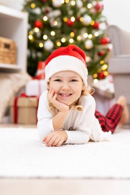 Evdeki Noel ağacının yanındaki halıda yatan küçük kız.