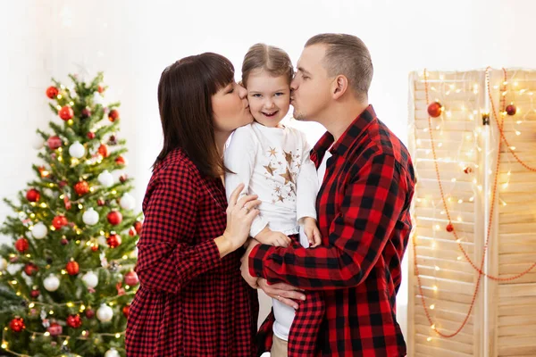 Föräldrar Håller Flicka Händer Och Kysser Henne Nära Julgran Hemma — Stockfoto
