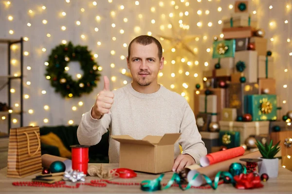 男とともにジェスチャー親指アップ座ってと包装クリスマスプレゼントに家 — ストック写真