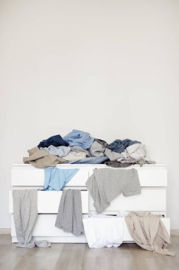 housework concept - chest of drawers with pile of dirty laundry, copy space over white wall background
