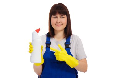Üniformalı ve sarı lastik eldivenli neşeli bir kadın. Elinde beyaz arka planda izole edilmiş tuvalet temizleyicisi olan plastik bir şişe tutuyor.