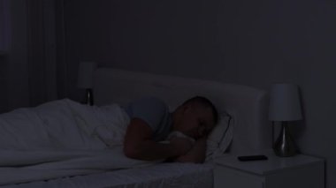 Uykusuzluk kavramı. Rahatsız, düşünceli bir adam. Geceleri karanlık bir yatak odasında tek başına yatıyor.