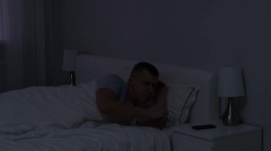 Genç adam akıllı telefonunun çalar saatini kapatmak için uyanıyor ve tekrar uykuya dalıyor. 