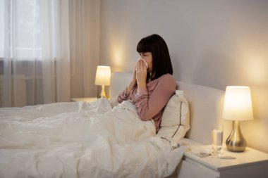 Genç hasta kadın evde yatarken burnunu siliyor.