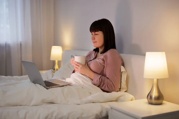 Mulher Usando Laptop Enquanto Deitada Sua Cama Com Xícara Bebida — Fotografia de Stock