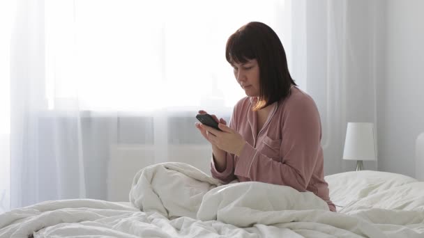 Молода Жінка Рожевій Піжамі Сидить Ліжку Використовує Смартфон Світлій Спальні — стокове відео