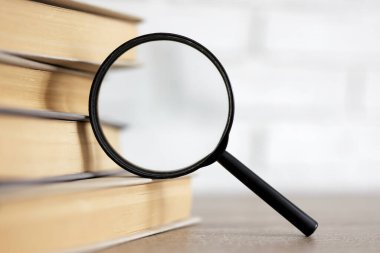 reading, education and research concept - stack of books and magnifying glass on the table in library