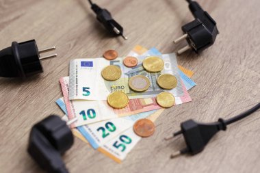 electricity cost and expensive energy concept - close up of electric power supply power cords plug with Euro banknotes and coins