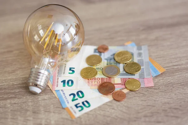 rise of electricity prices concept - light bulb with Euro banknotes and coins