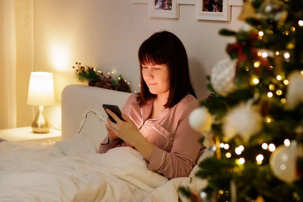 Portrét Mladé Ženy Pomocí Smartphonu Zdobené Ložnici Vánoční Stromeček — Stock fotografie