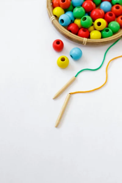 toy for motor skills development - close up of colorful wooden beads, lace and needle over white background with copy space