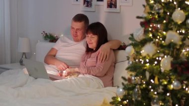 Ev, aile ve Noel konsepti. Mutlu çift film izliyor ve Noel ağacının yanında patlamış mısır yiyor.