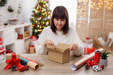 Kadın, Noel süslemeli bir odada masanın başında oturmuş kutunun içine bakıyor.