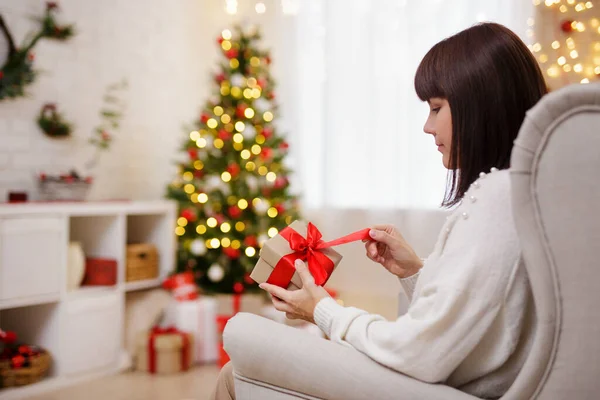 女性座っているアームチェアとオープンギフトでクリスマス装飾された部屋 — ストック写真