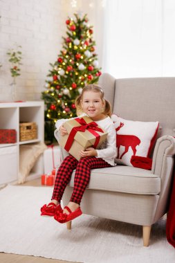 Mutlu küçük kız Noel süslemeli odada bir hediye tutuyor.