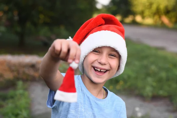 A laughing boy in a Santa hat holds a small Santa helper hat in his hand. — Stock Photo, Image