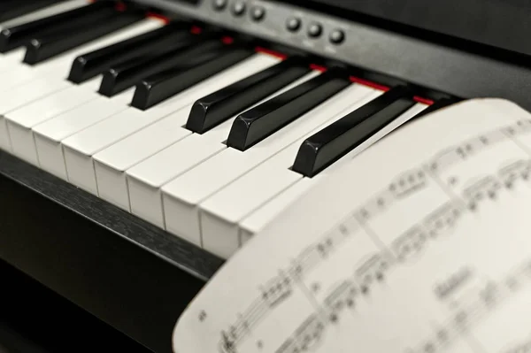 Primo piano dei tasti elettronici del pianoforte. foglio di carta con note musicali. — Foto Stock