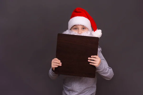 Santa boy holds an empty sign for the inscription. on a gray background. mock up — Stock Photo, Image