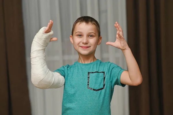 O rapaz levantou as duas mãos. Um braço está quebrado em um molde. — Fotografia de Stock
