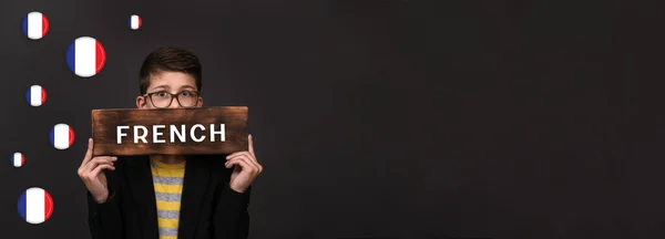 Apprendre le français. bannière sur fond noir. un adolescent tient un panneau publicitaire pour les cours de langue. espace de copie — Photo