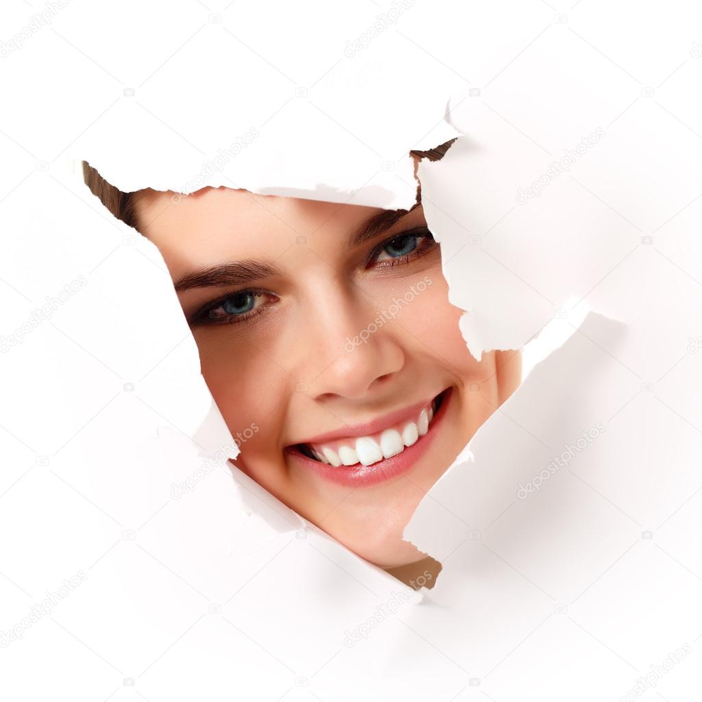 cheerful teen girl peeping surprised through hole in white paper