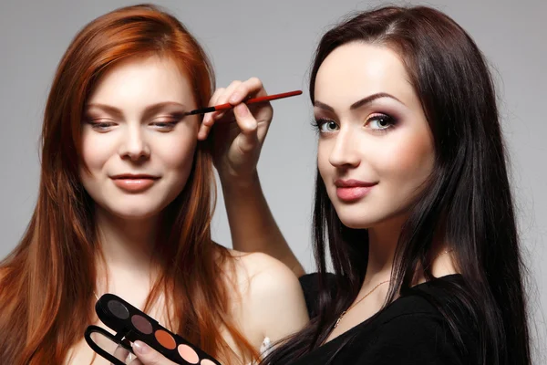 Retrato de una hermosa joven pelirroja con esteticista haciendo sombra de ojos de maquillaje —  Fotos de Stock