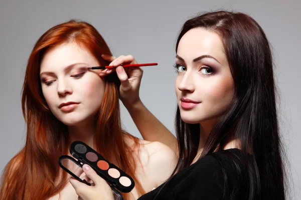 Retrato de una hermosa joven pelirroja con esteticista haciendo sombra de ojos de maquillaje —  Fotos de Stock