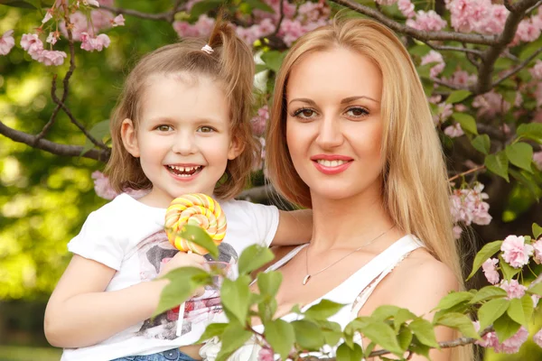 Happy mother with little daughter licks candy spring park outdoor — Stock Photo, Image