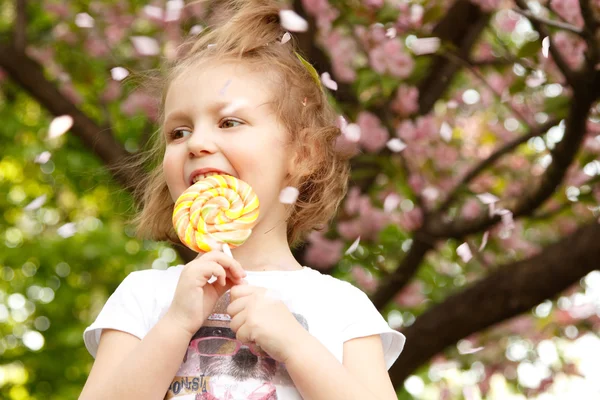 Happy little girl licks sweet candy nature outdoor — Stock Photo, Image