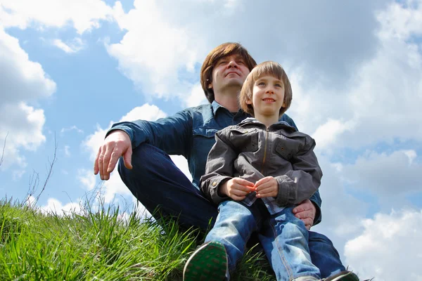 Feliz padre con pequeño hijo sentado en la hierba verde y mirando en el futuro —  Fotos de Stock