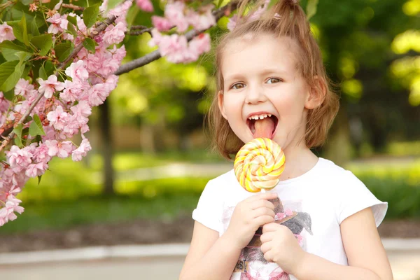 Happy little girl licks sweet candy nature summer outdoor — Stock Photo, Image