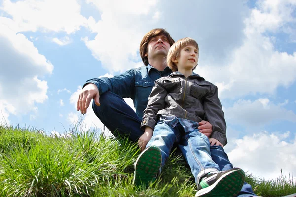 Feliz padre con pequeño hijo sentado en la hierba verde y mirando en el futuro — Foto de Stock