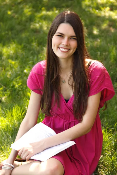 Atractivo feliz sonriente estudiante adolescente leyendo libro en el parque —  Fotos de Stock