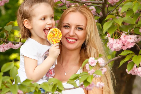 Šťastné matky s malou dcerou olizuje candy jaro park venkovní — 图库照片
