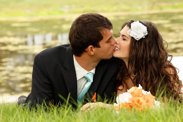 Young bride and groom lying on green grass — Stock Photo, Image