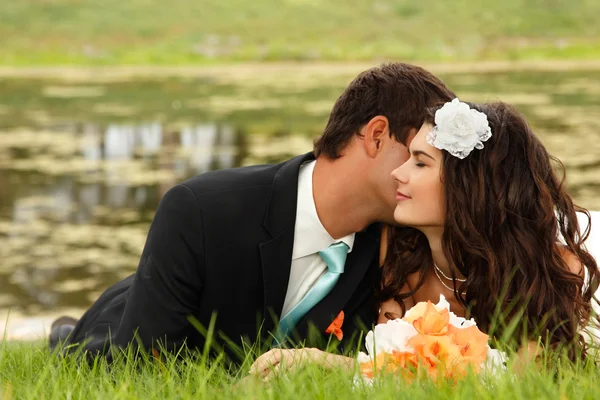 Young bride and groom lying on green grass — Stock Photo, Image