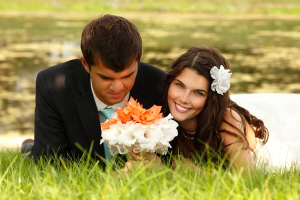 Mladá nevěsta a ženich leží na zelené trávě — Stock fotografie