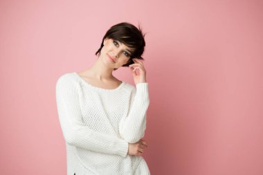 Stüdyoda pembe arka planda poz veren güzel esmer kadın kameraya bakıyor ve düşünüyor, hayaller kuruyor, gelecek için planlar yapıyor.