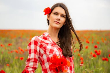 Genç, güzel, neşeli bir kadın bahar tarlasında çiçek açan gelinciklerin arasında yürüyor..