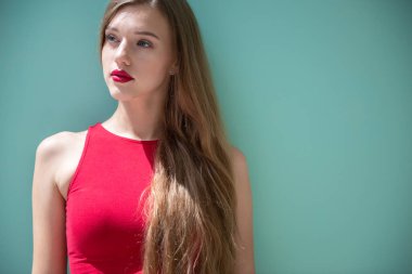 Uzun sarı saçlı, mavi kot pantolon giyen ve açık mavi-yeşil arka planda kırmızı bluzlu güzel bir kadın.. 