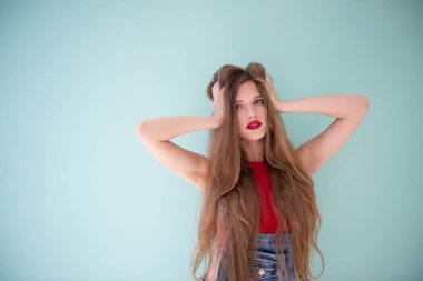 Uzun sarı saçlı, mavi kot pantolon giyen ve açık mavi-yeşil arka planda kırmızı bluzlu güzel bir kadın.. 