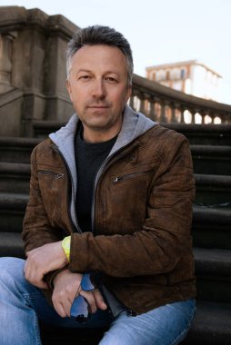 Baharda sokak tarzı kot pantolon ve kahverengi ceket giyen yakışıklı bir adamın şehir dışı portresi.