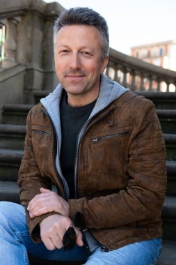 Baharda sokak tarzı kot pantolon ve kahverengi ceket giyen yakışıklı bir adamın şehir dışı portresi.