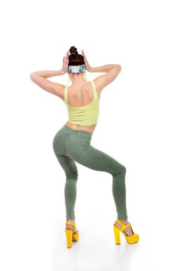 Sokak kıyafeti giyen, sarı topuklu sandalet giyen, beyaz arka planda dans eden genç moda çekici kız.