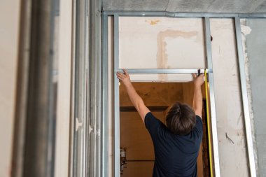 Erkek işçi ses geçirmez oda için alçıpan profili ekliyor. İnşaat işleri, tamirat. Yenileme