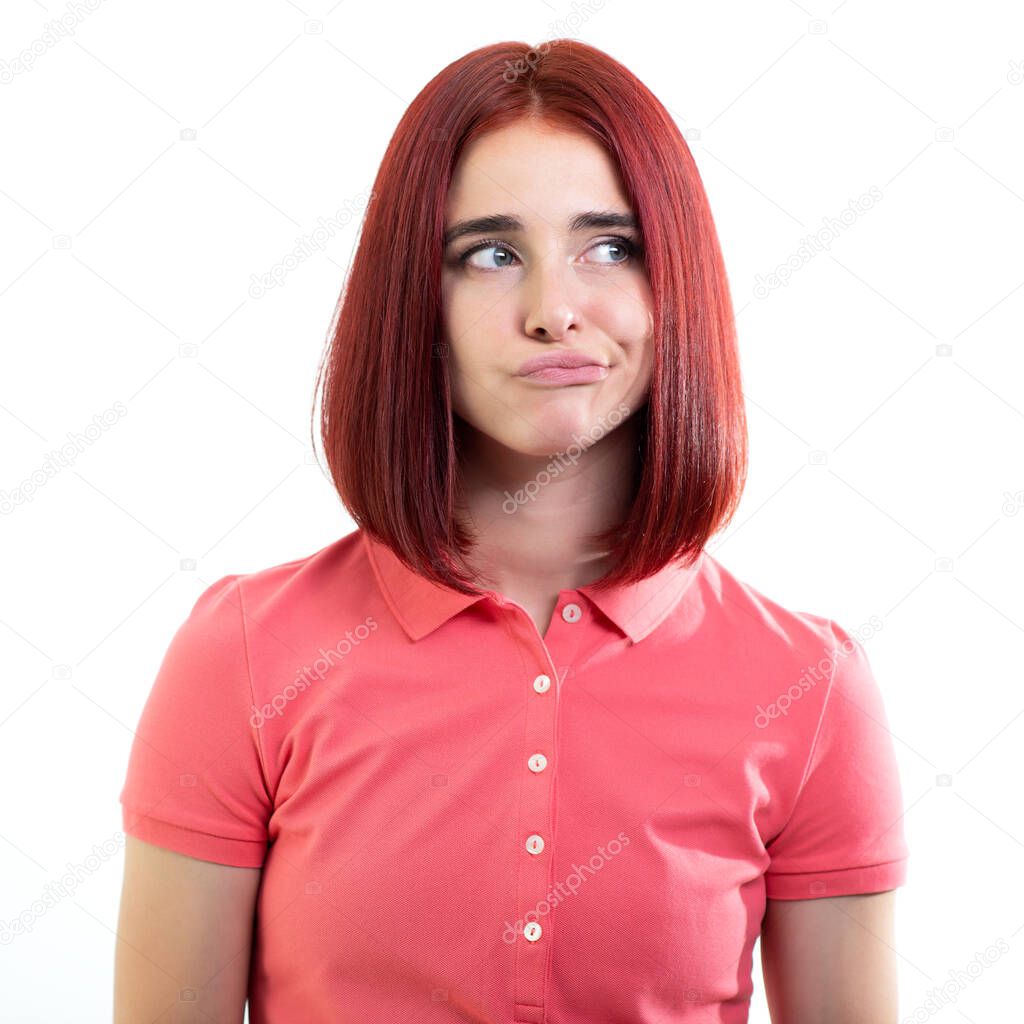 Young ginger woman wearing pink t-shirt using facial expressions to say doubts, discontent, uncertainty about the future, regret, failure, fail, helplessness, studio shot over white background. 