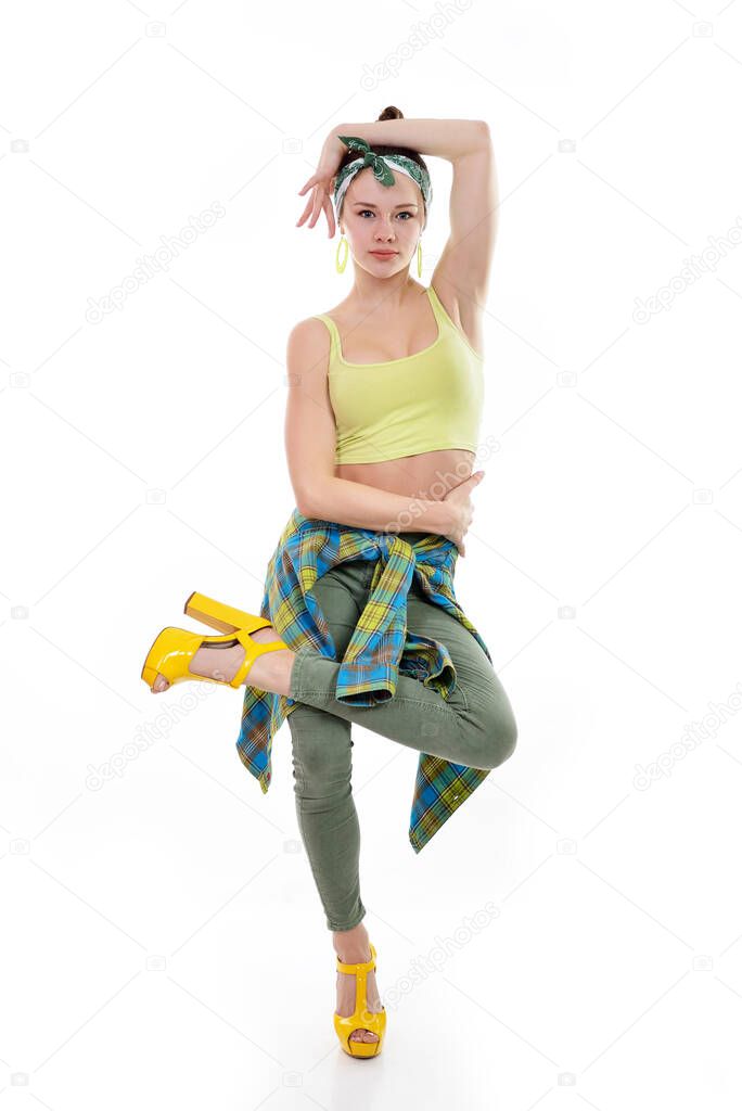 Young fashion charming girl wearing streetwear and yellow high heel sandals dancing at studio on a white background