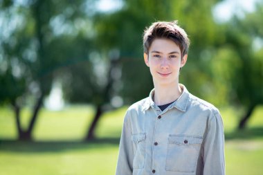 Yakışıklı, neşeli, 15 yaşında, gülümseyen ve mavi gökyüzüne, ağaçlara ve ilkbahar çayırında yeşil çimenlere bakan bir çocuk.. 