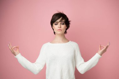 Genç ve güzel bir kadın pembe arka plan üzerinde meditasyon yapıyor. Rahatlama, piritüel uygulama ve yoga.