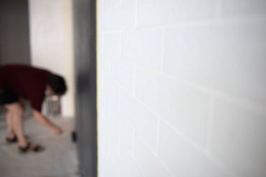 Patenli duvar boyası. İşçi duvarı boyar, evi elden geçirir, beyaz tuğlalara odaklanır. Ressam iş başında. Ev yenilenmesi